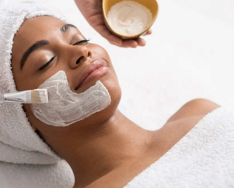 A treatment mask being brushed onto a client's face during a Clean Skin facial